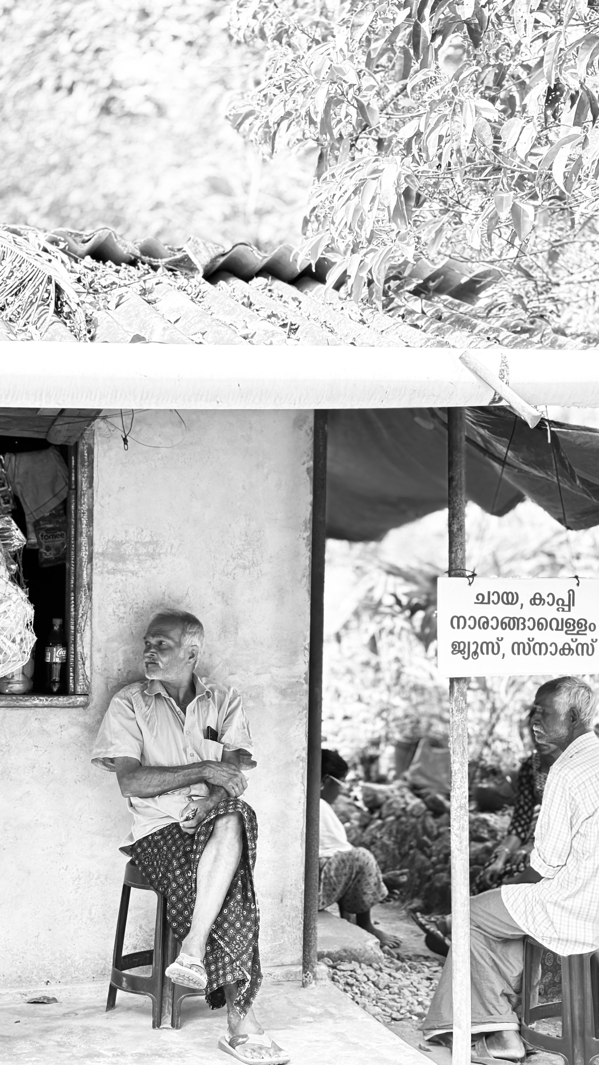 Black and white photo of an elderly man seated at a rustic tea stall in Idukki, Kerala.