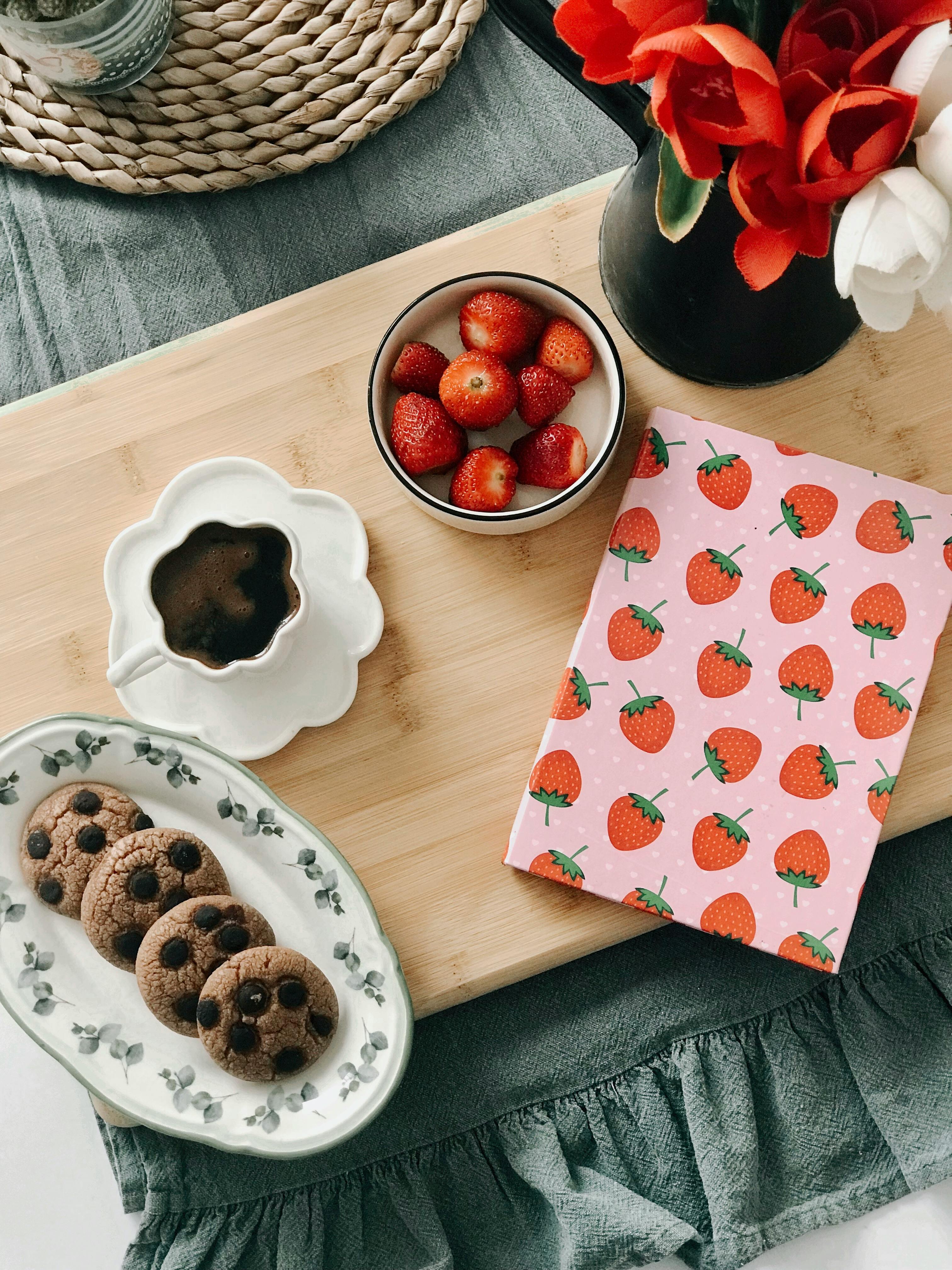 Cozy breakfast setting with cookies, coffee, strawberries, and flowers on a wooden tray.