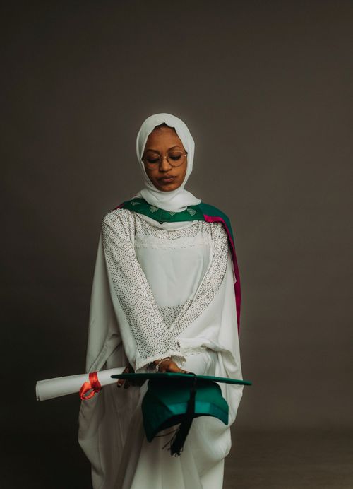 Free Young woman in graduation gown and hijab holding a diploma, symbolizing academic achievement. Stock Photo