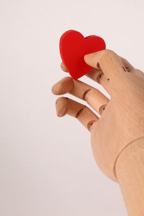 Free A wooden mannequin hand gently holds a red heart symbolizing love and emotion. Stock Photo