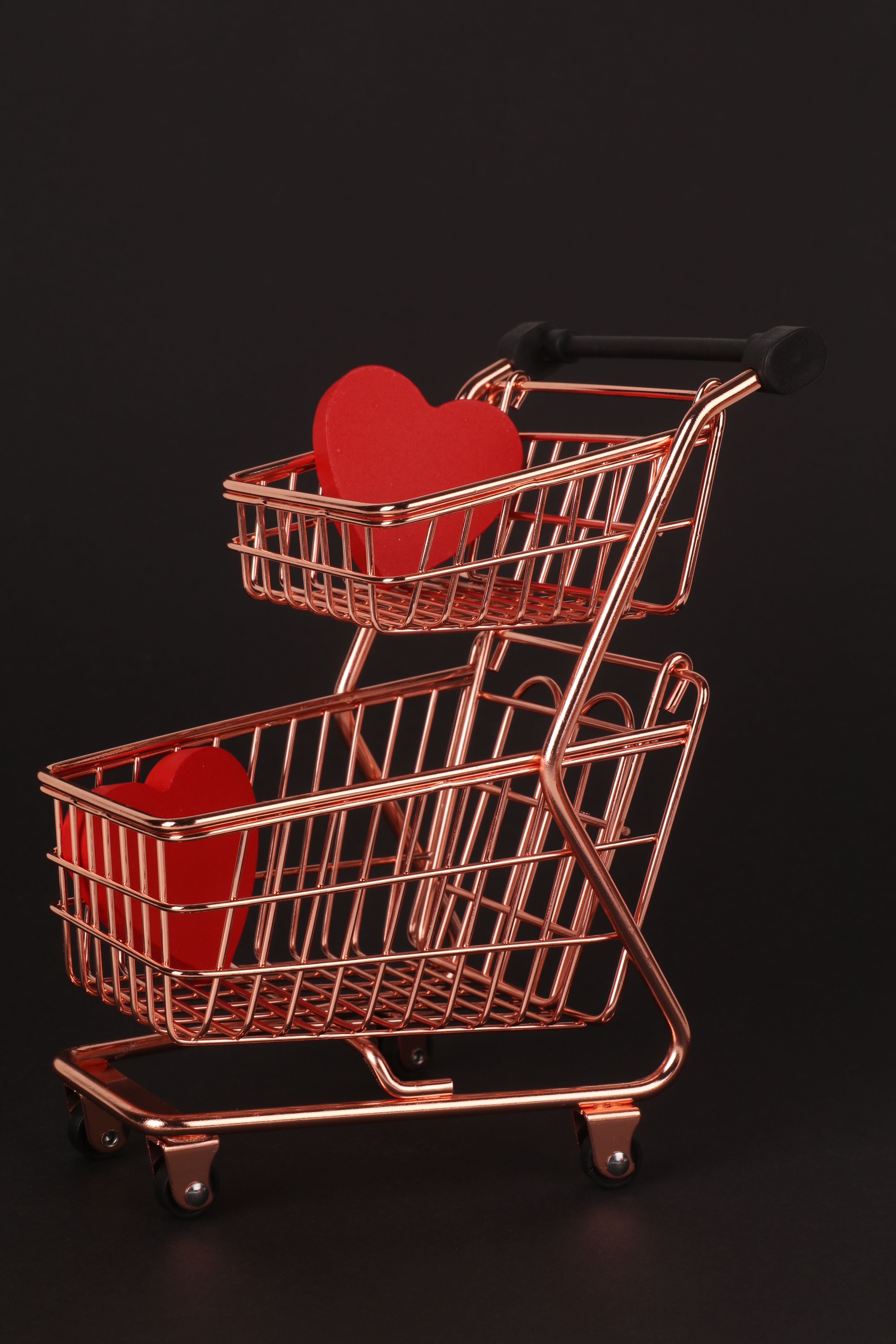 Copper shopping cart holding red hearts on a black backdrop, symbolic of love and shopping.