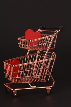 Copper shopping cart holding red hearts on a black backdrop, symbolic of love and shopping.