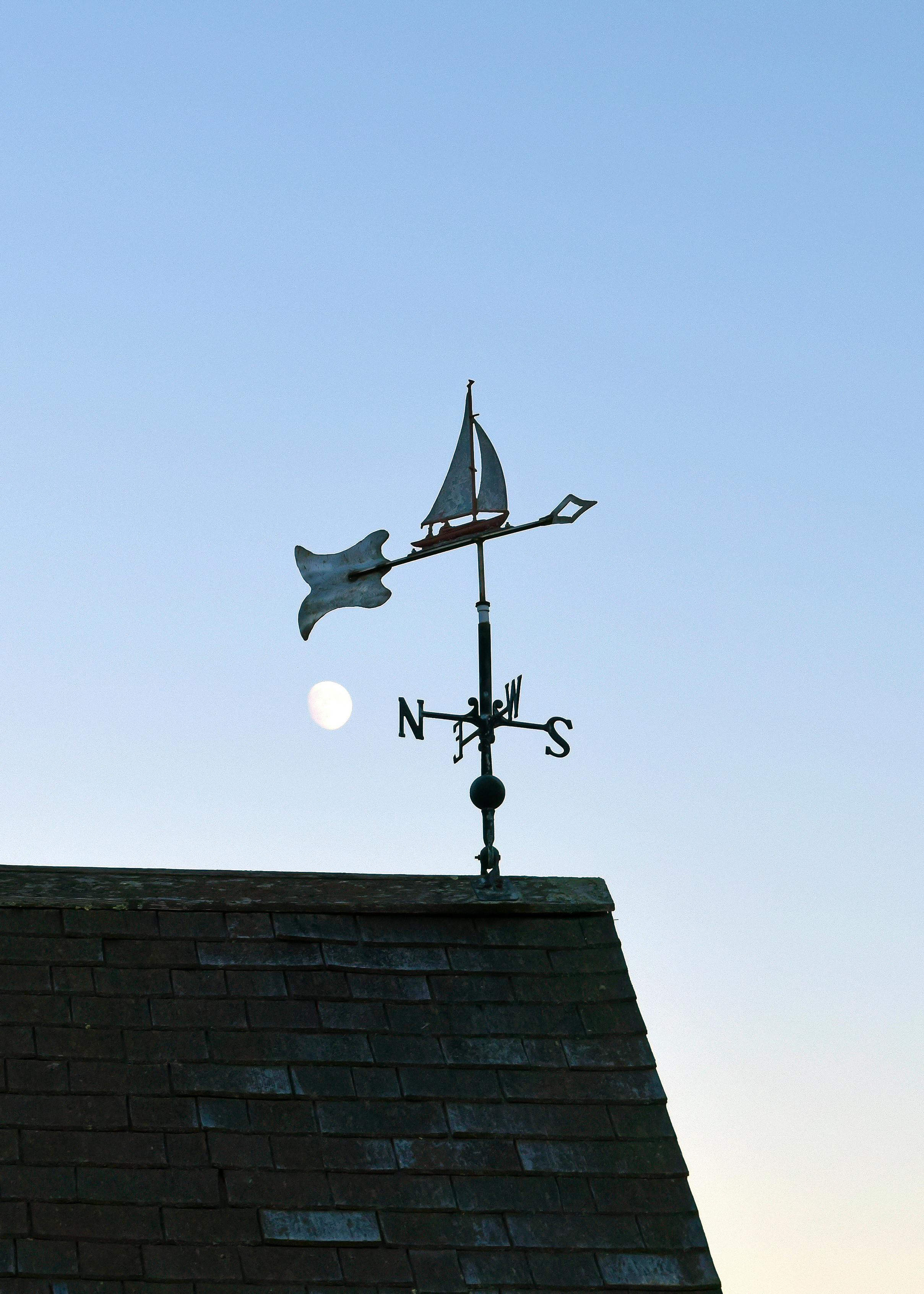A nautical weather vane depicting a sailboat under the moonlit sky on a rooftop.