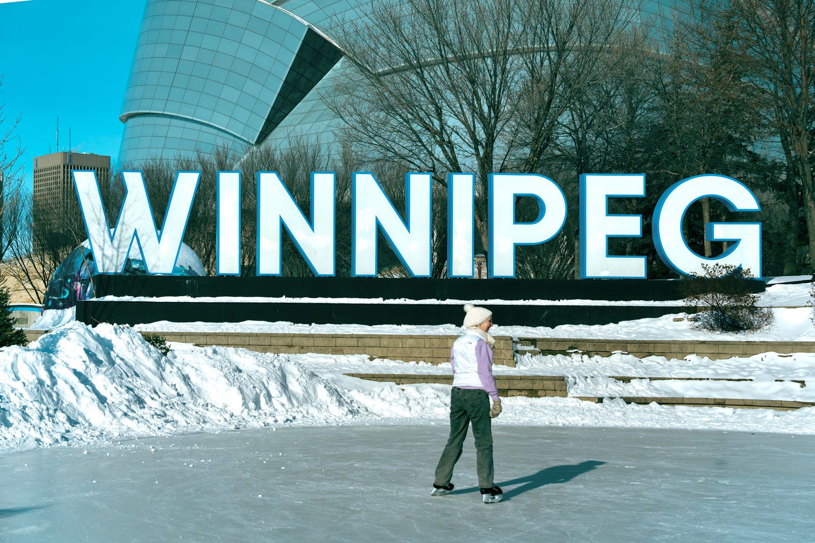 Skater on an outdoor ice trail beside the Winnipeg sign in winter