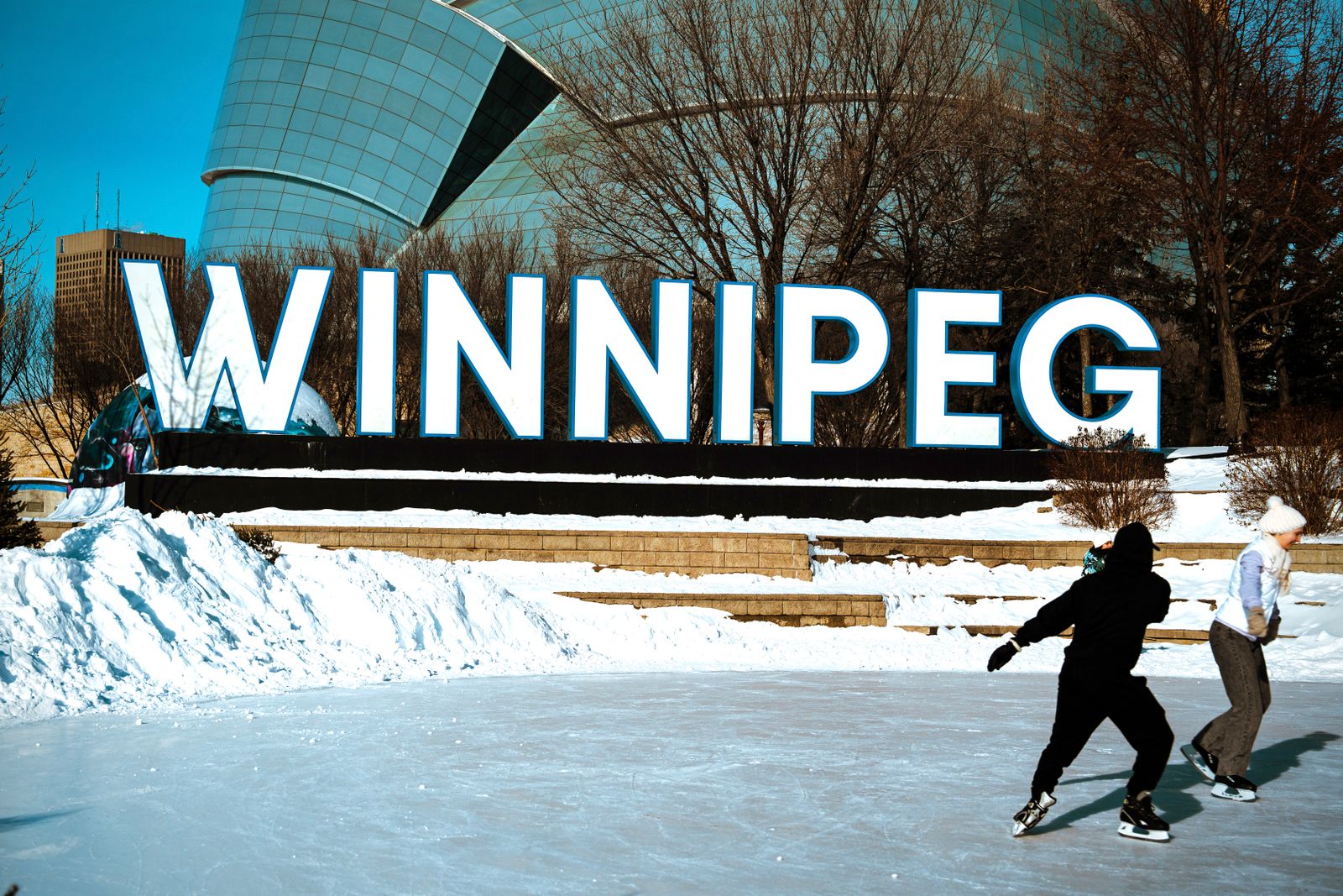 People skating on an outdoor rink in front of the Winnipeg sign on a clear winter day