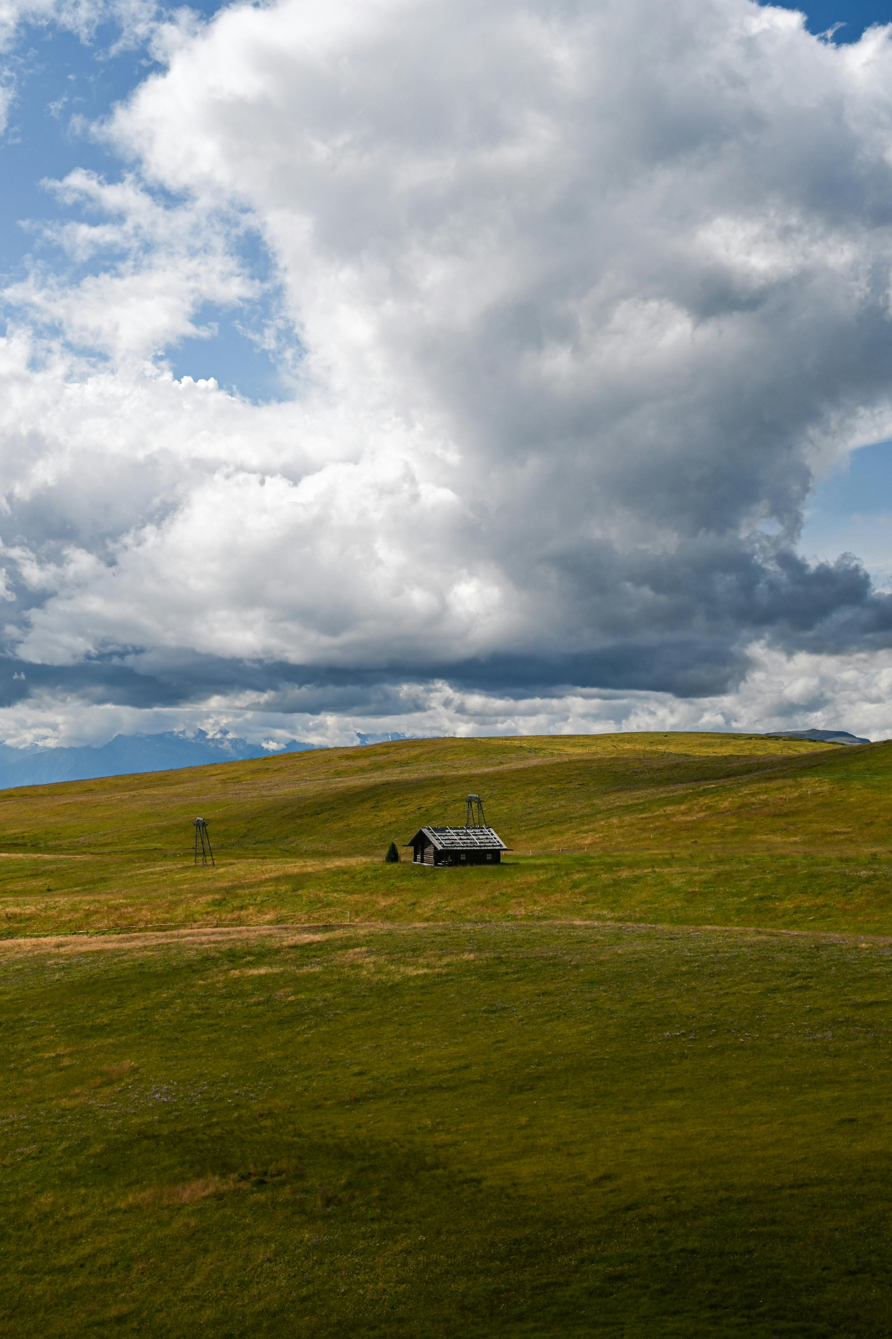 A solitary cabin sits on expansive grasslands beneath a dramatic cloudy sky.