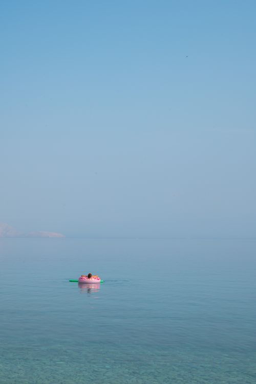 Free A person floats on an inflatable ring in a calm sea under a clear blue sky. Stock Photo