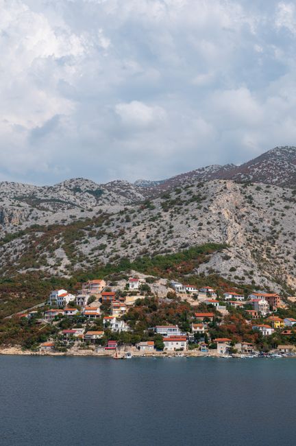 Scenic coastal village surrounded by rocky hills and a tranquil sea under a cloudy sky.