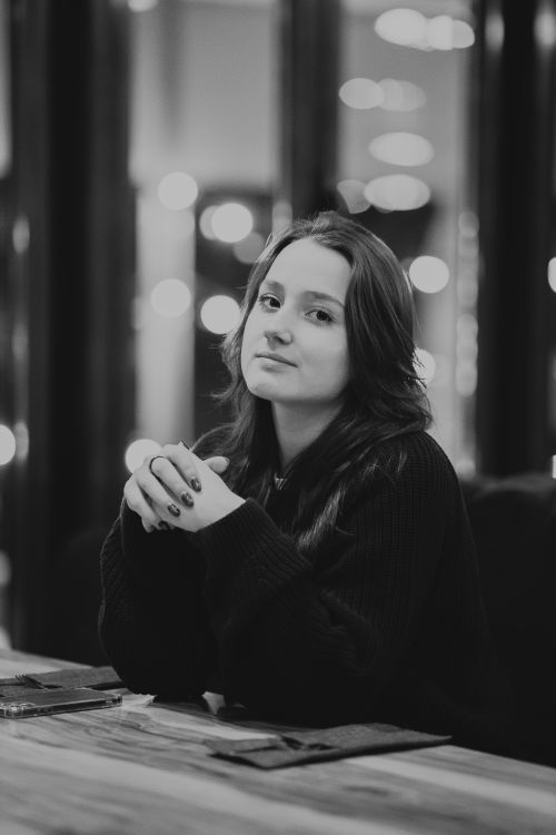 Free Monochrome portrait of a young woman sitting in a dimly lit setting with bokeh lights. Stock Photo