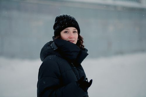 Free A woman in a winter coat smiling warmly in a snowy outdoor setting. Stock Photo