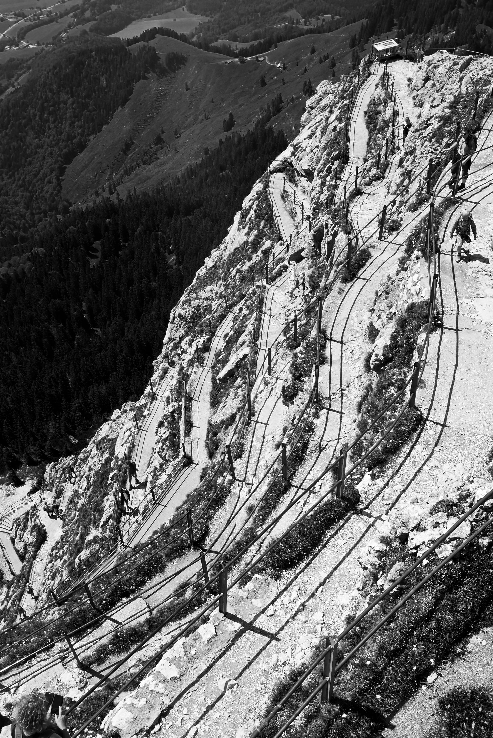 Black and white image of a winding mountain path with secure railings offering a breathtaking view.
