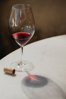 A wine glass with red wine on a marble table, casting a shadow.