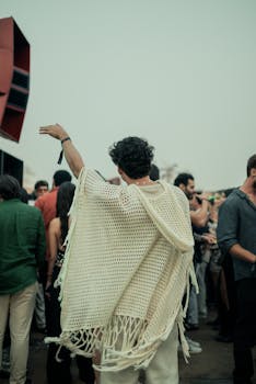 A lively crowd enjoying an outdoor music festival, person in front raising hand.
