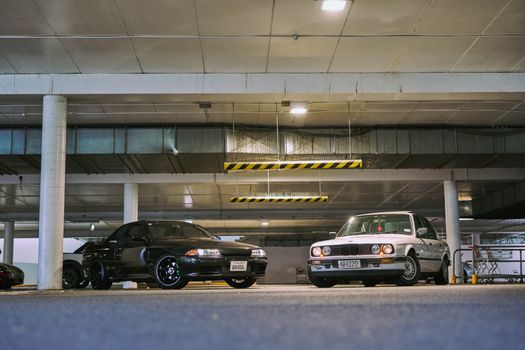 Two vintage modified cars showcasing modifications in an Auckland parking garage.