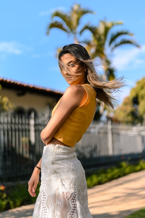 Foto De Vista Lateral De Mujer En Top Corto Sin Mangas Amarillo Y Vestido Blanco Posando