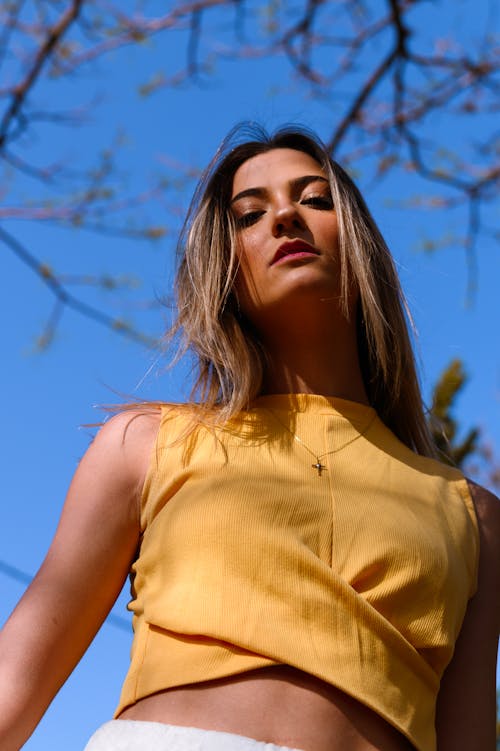 Low Angle Photo of Woman in Yellow Crop Top Posing While Looking Down