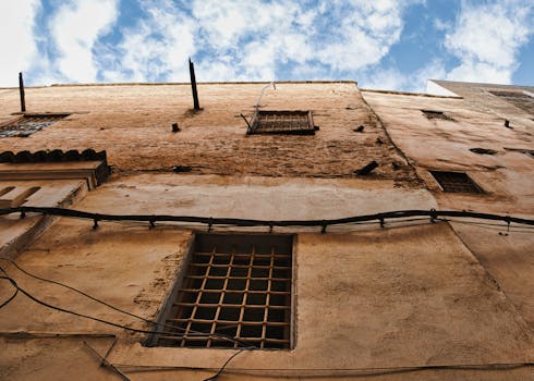 Upward view of a weathered wall in Fes Medina with a blue sky backdrop.
