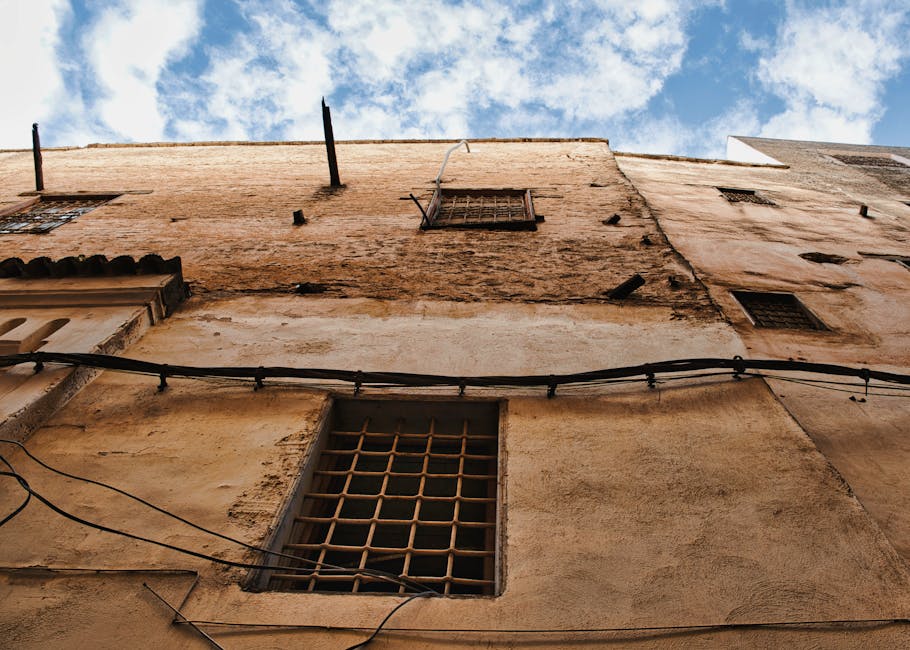 Upward view of a weathered wall in Fes Medina with a blue sky backdrop.