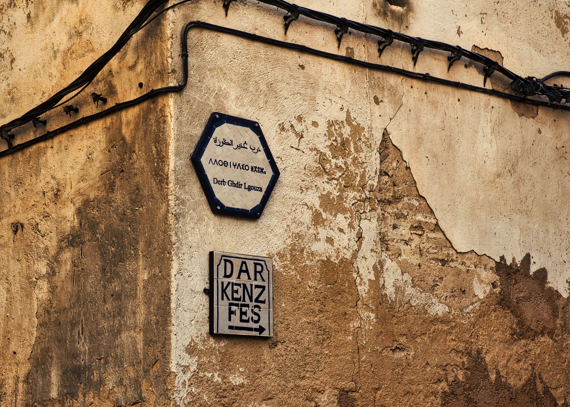 Street signs on a rustic wall in the medina of Fes, Morocco, showcasing cultural heritage.