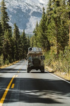 一辆车沿着风景优美的森林道路行驶，背景是山脉，画面捕捉了自由与冒险的感觉