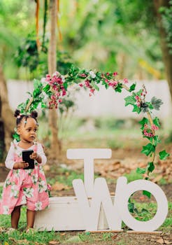A charming toddler celebrates their second birthday in a floral outdoor setting.