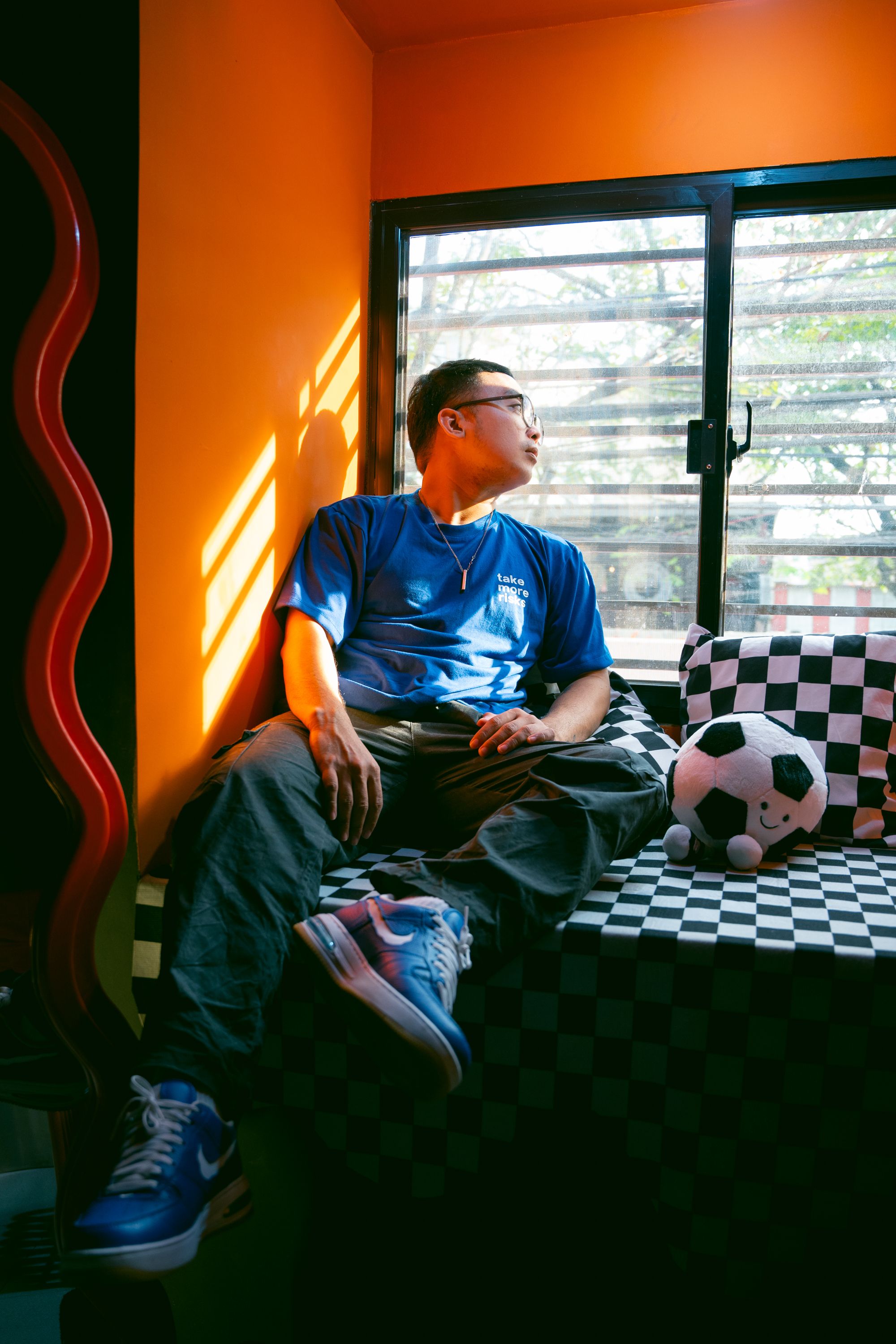 A man sitting by the window in a vibrant room with checkered decor and sunlight streaming in.