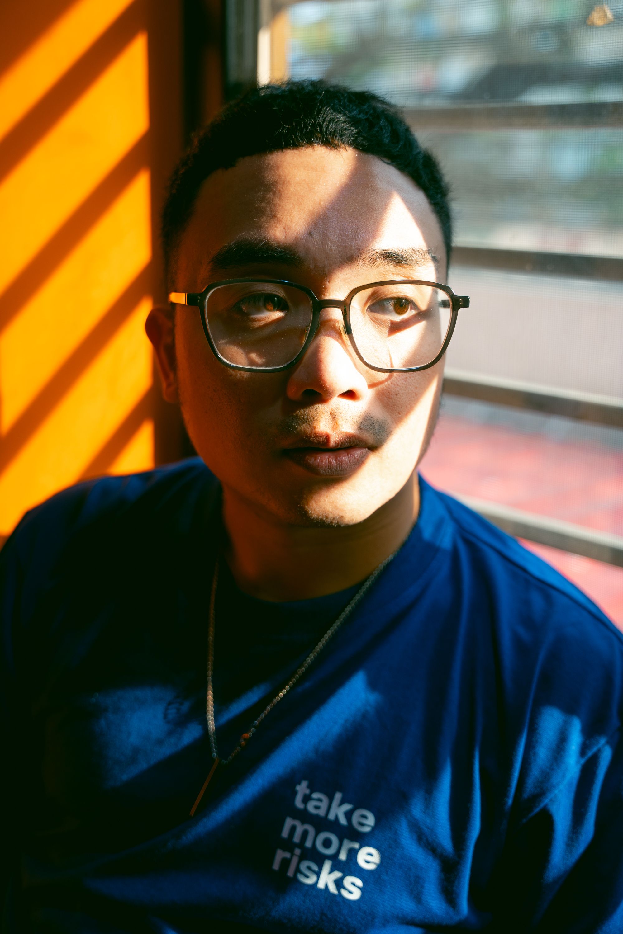 Young man in inspirational blue shirt poses in sunlight indoors.