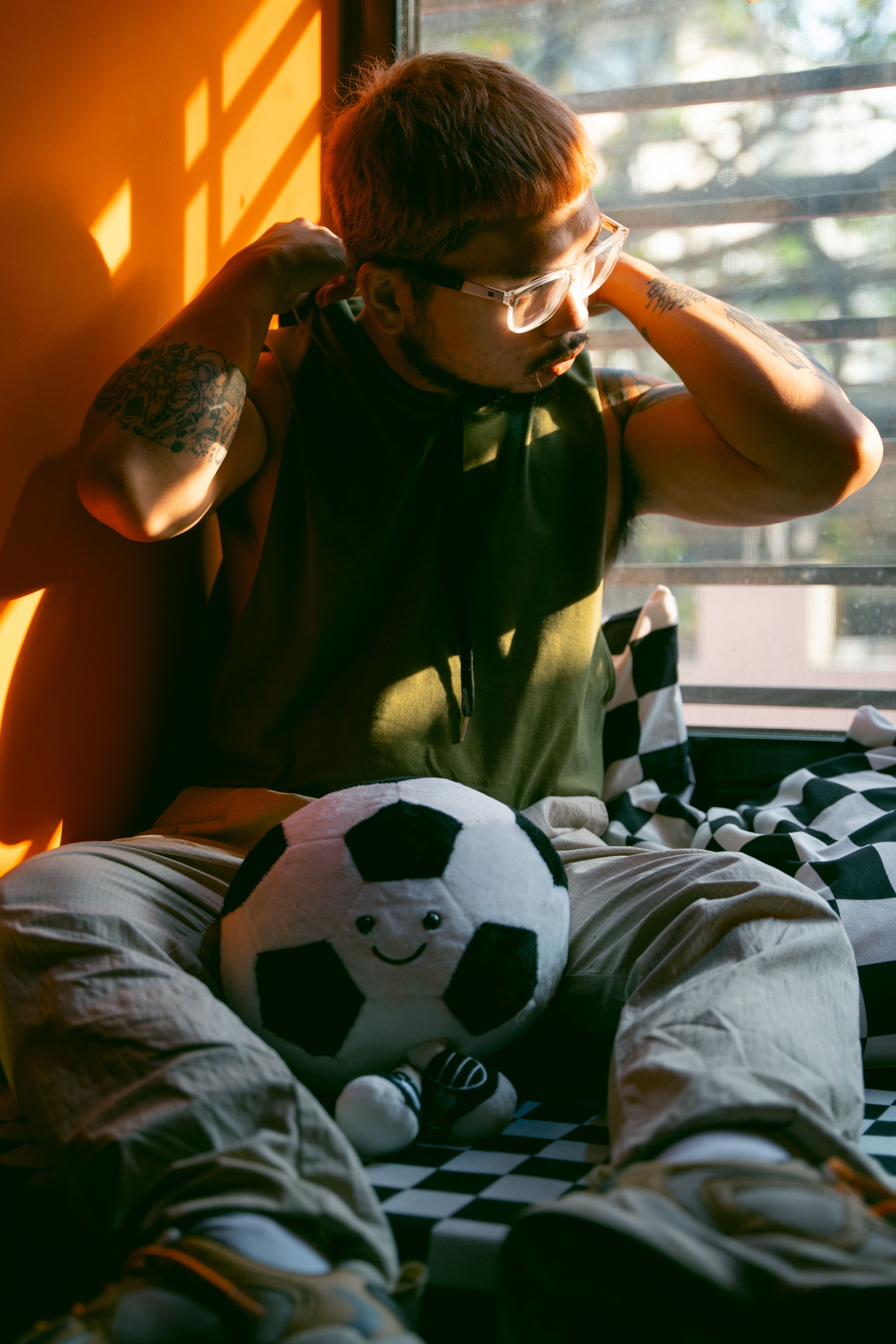 A person sits by the window, adjusting headphones, with a soccer ball in a warmly lit room.