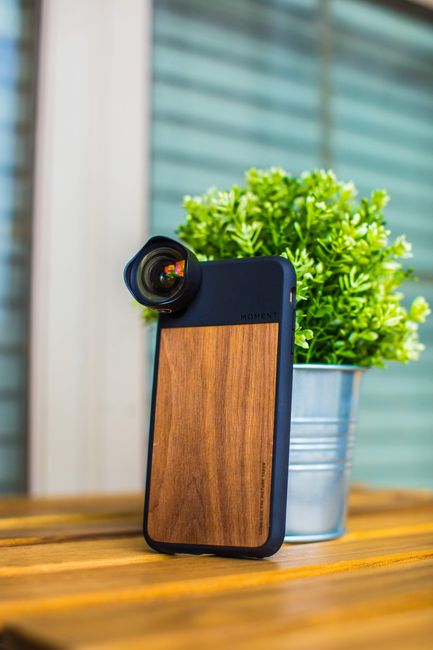 Close-up of smartphone with wooden case and lens attachment beside a potted plant. - mobile accessories Pakistan
