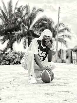 Black and white photo of a young man posing with a basketball outdoors in OS, Nigeria.