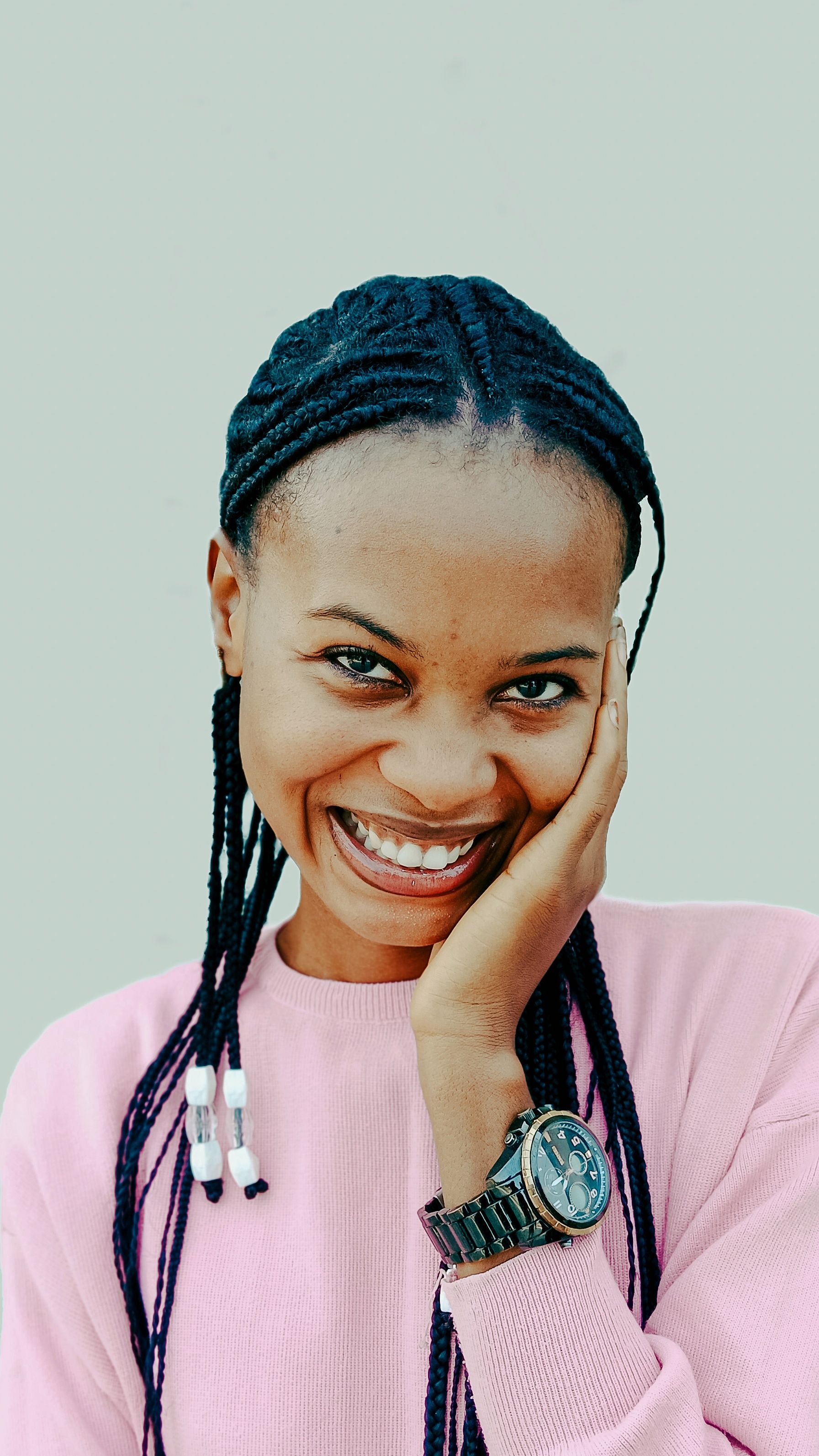 Portrait of a young woman smiling warmly, showcasing a braided hairstyle against a plain background.