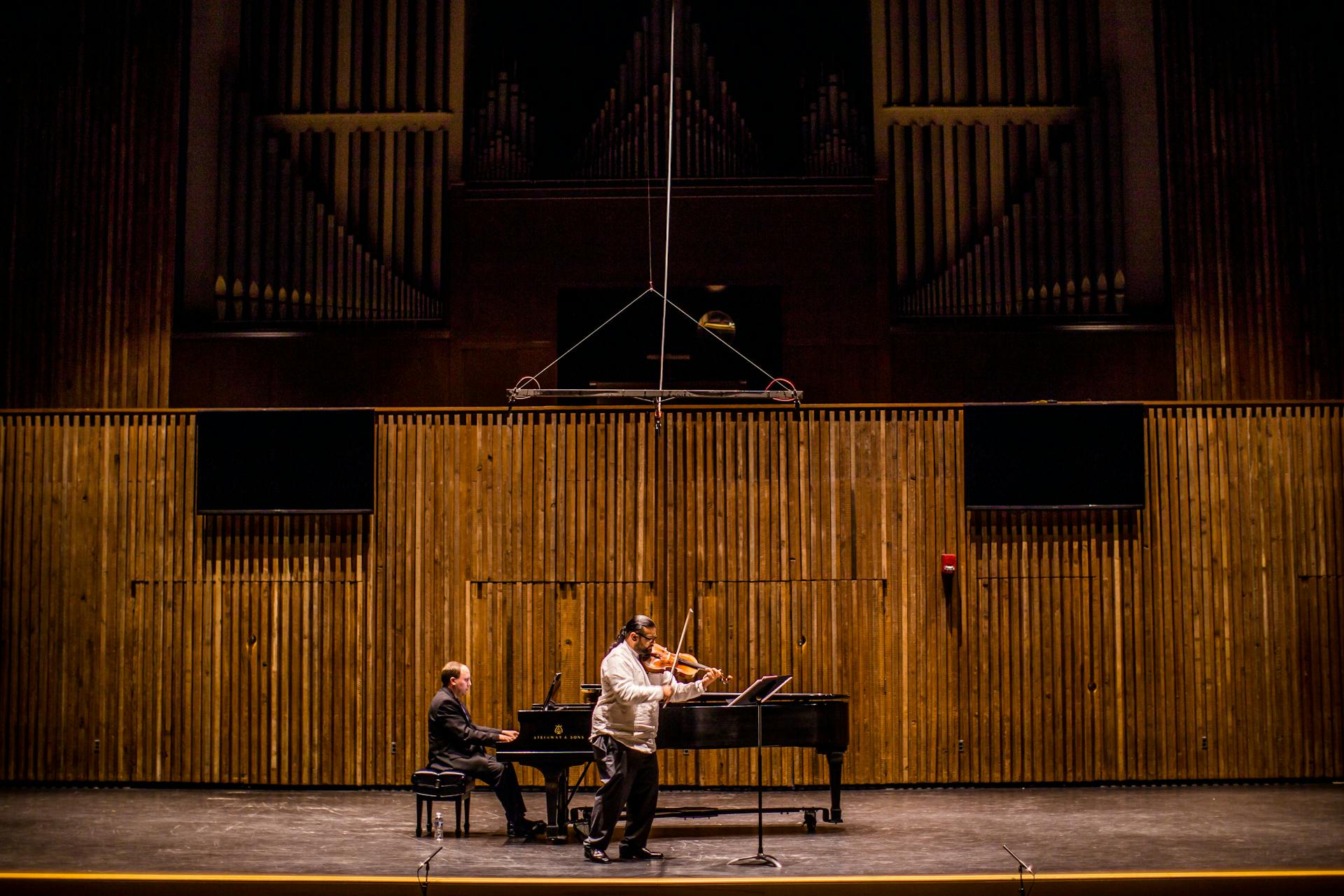 Two musicians perform piano and violin on stage in a concert hall.