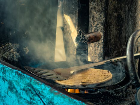 A rustic scene of flatbread cooking on an open flame with a spatula.