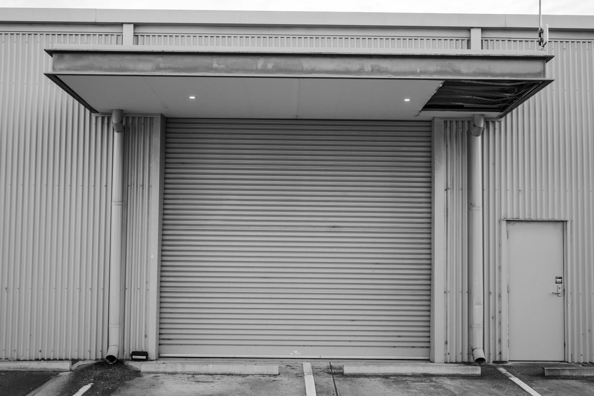 Black and white image of a closed industrial garage door with corrugated metal exterior.