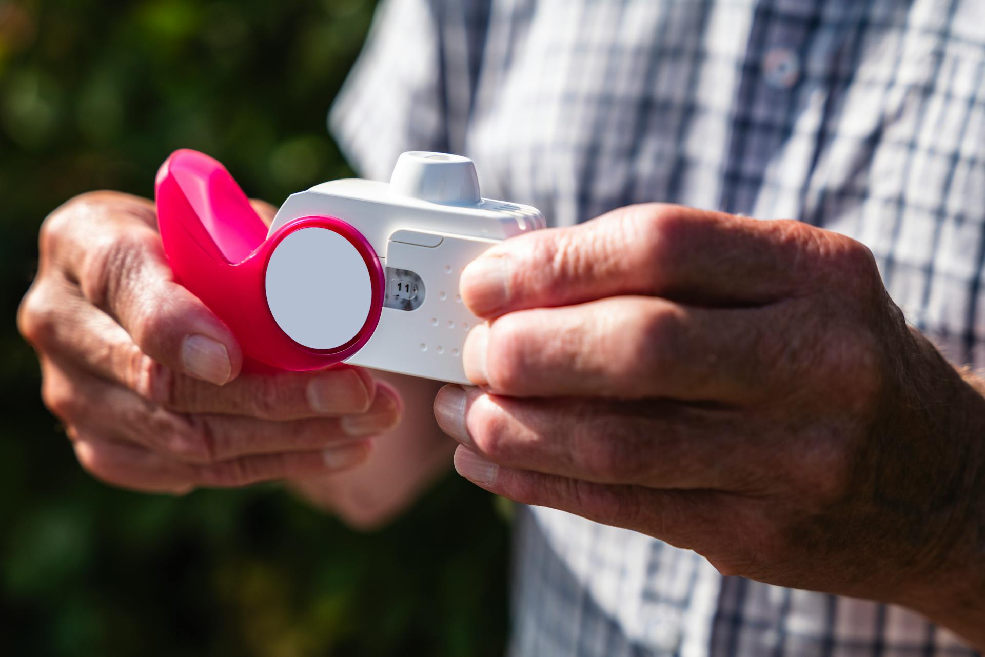 Close-up of senior hands holding an inhaler outdoors, showcasing health and respiratory care.