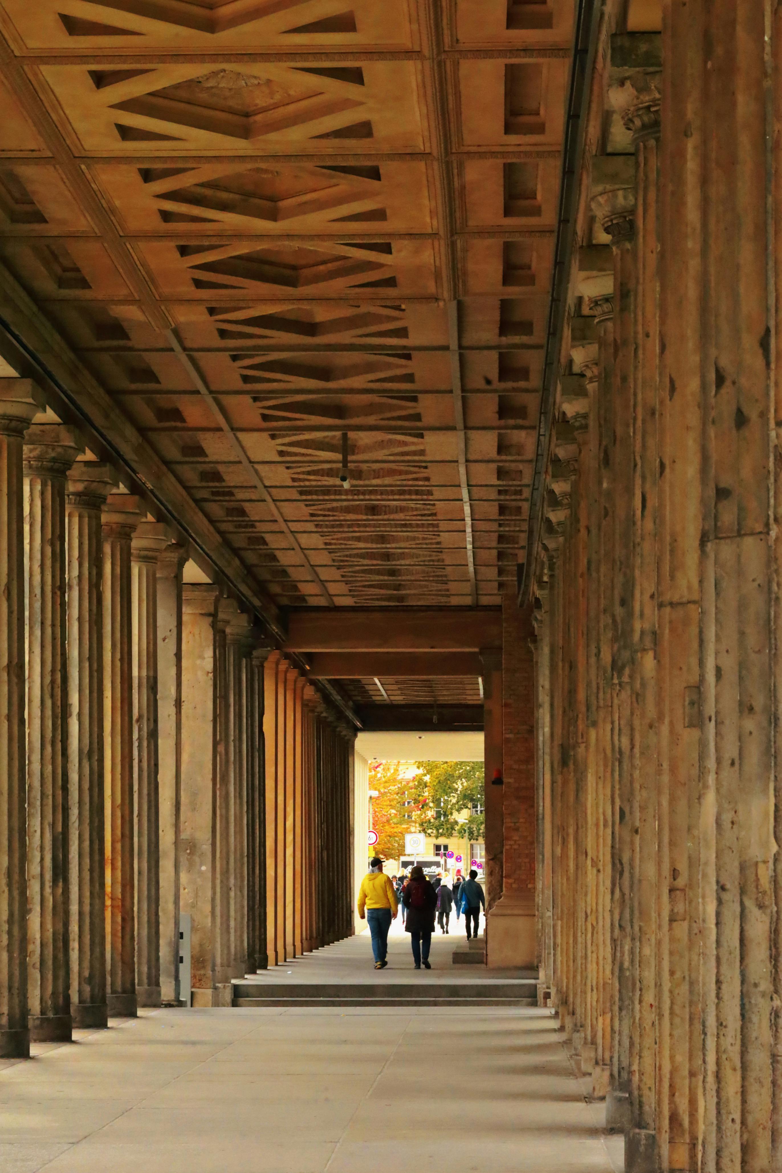 People strolling through historic columns in Berlin, Germany during autumn.