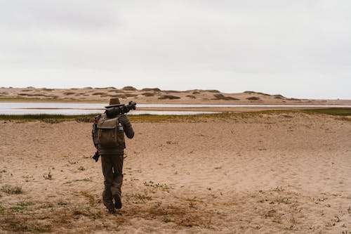 Man Walking With A Backpack And Camera Equipment On Sandy Ground