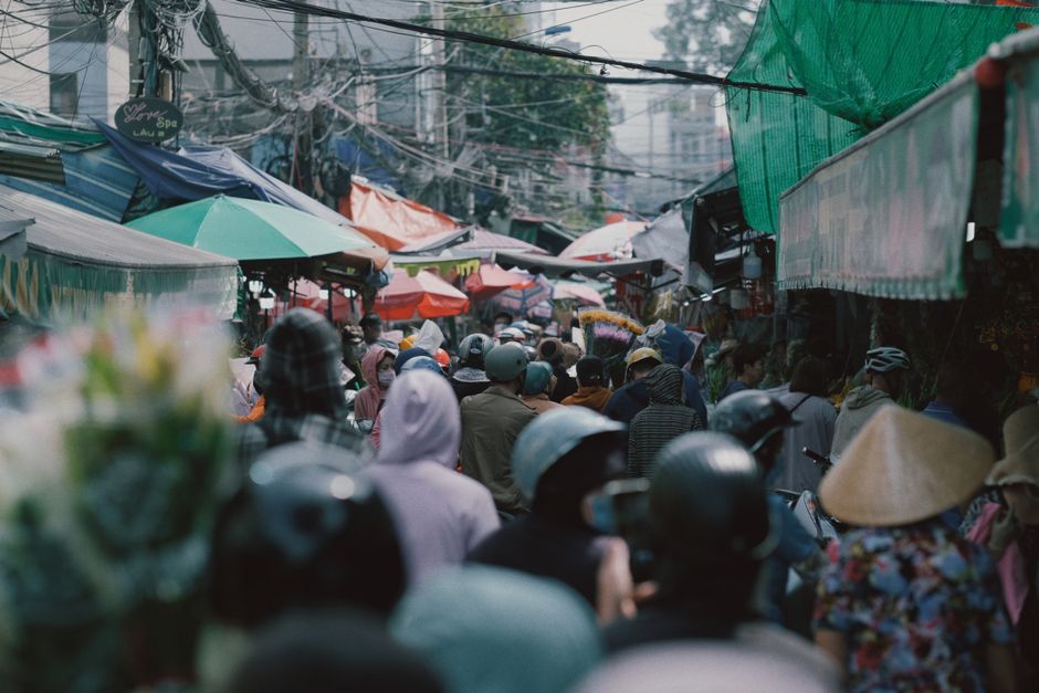 Bustling outdoor market scene with diverse vendors and shoppers under colorful canopies.