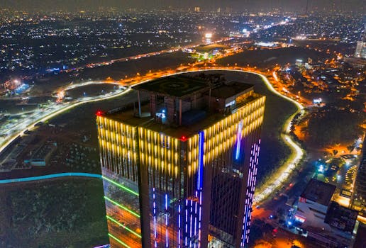 夜间，从空中俯瞰一座灯火通明的摩天大楼，矗立在繁忙的城市中
