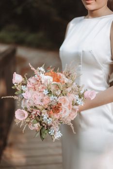 Elegant bridal bouquet held by a bride in an outdoor setting, showcasing pastel florals.