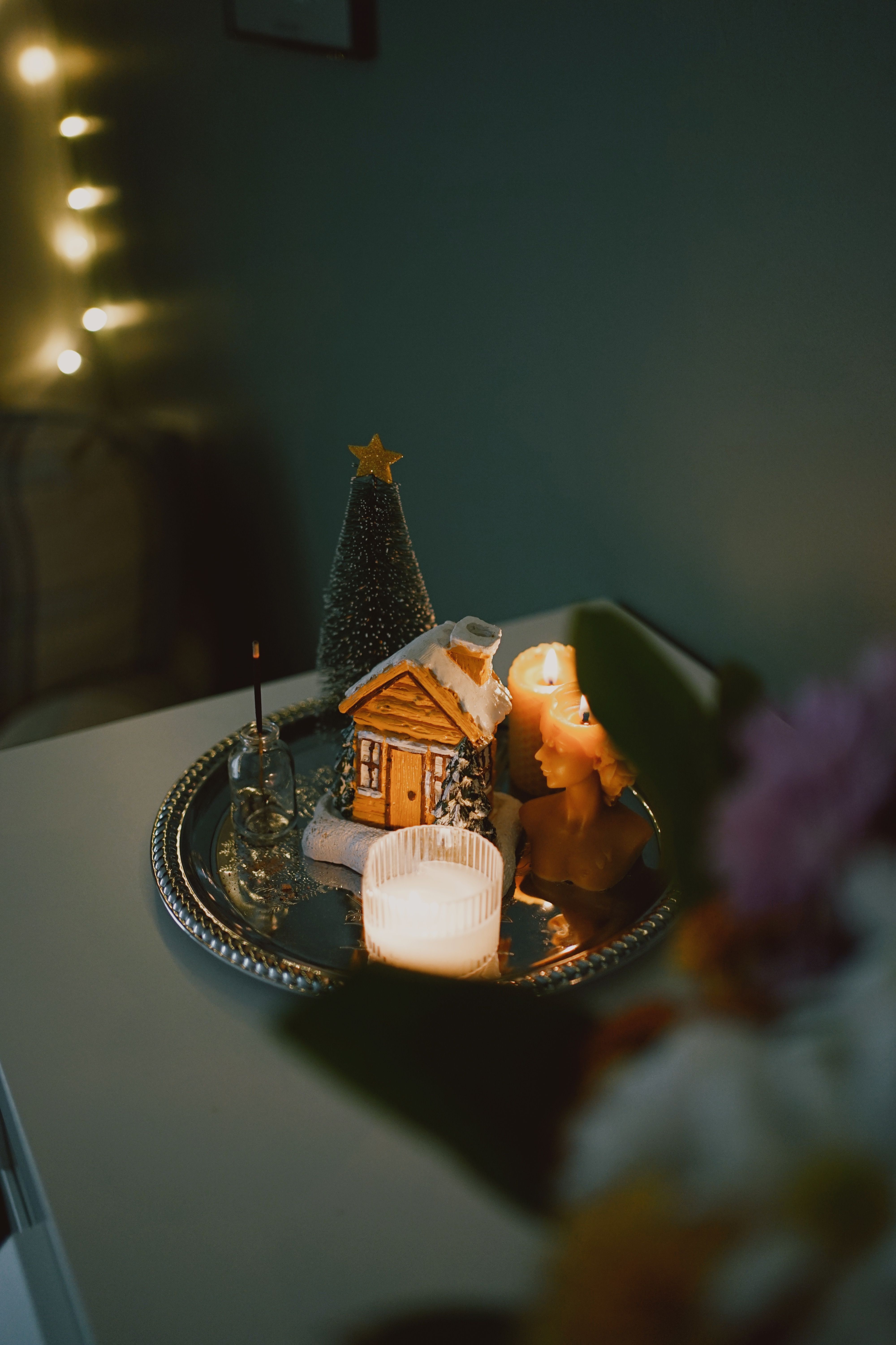Warm candlelit decorative setting with miniature house, Christmas tree, and glowing lights.