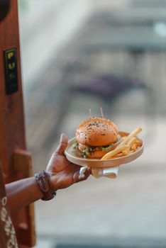 A close-up of a hand holding a plate with a gourmet burger and fries, perfect for food blogs.