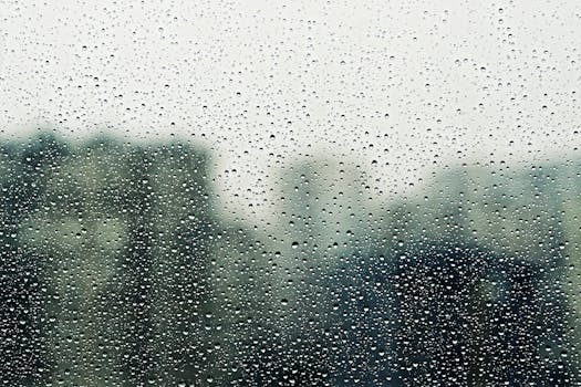 Close-up of raindrops on a window with blurred background, conveying a moody, cozy vibe.