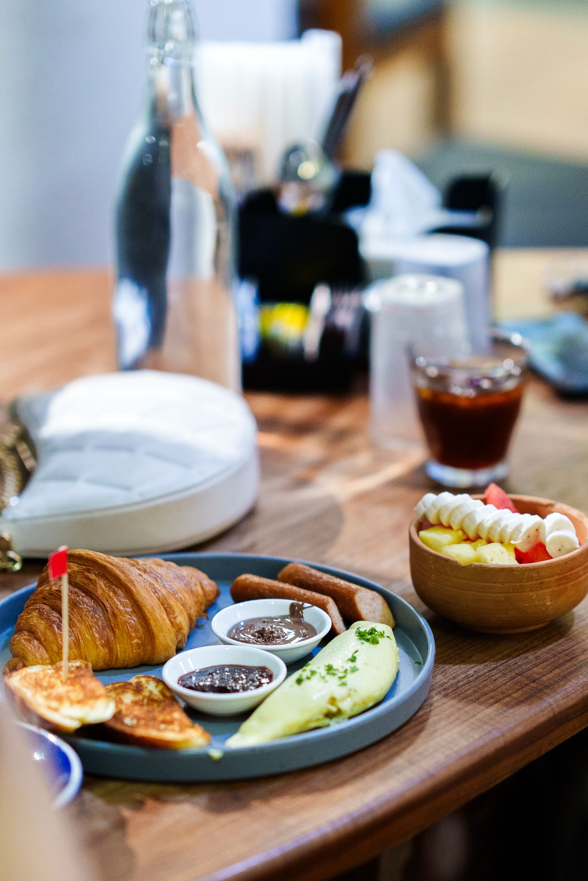 Tasty breakfast with croissant, fruits, and jams on a wooden table setting.