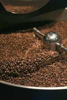 Close-up of roasted coffee beans in an industrial coffee roaster with metallic scoop.