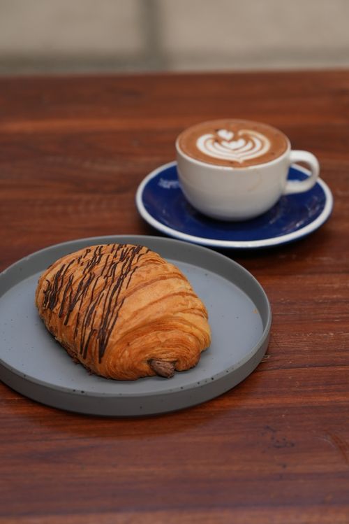 Free Close-up of a chocolate croissant with cappuccino on a wooden table. Stock Photo