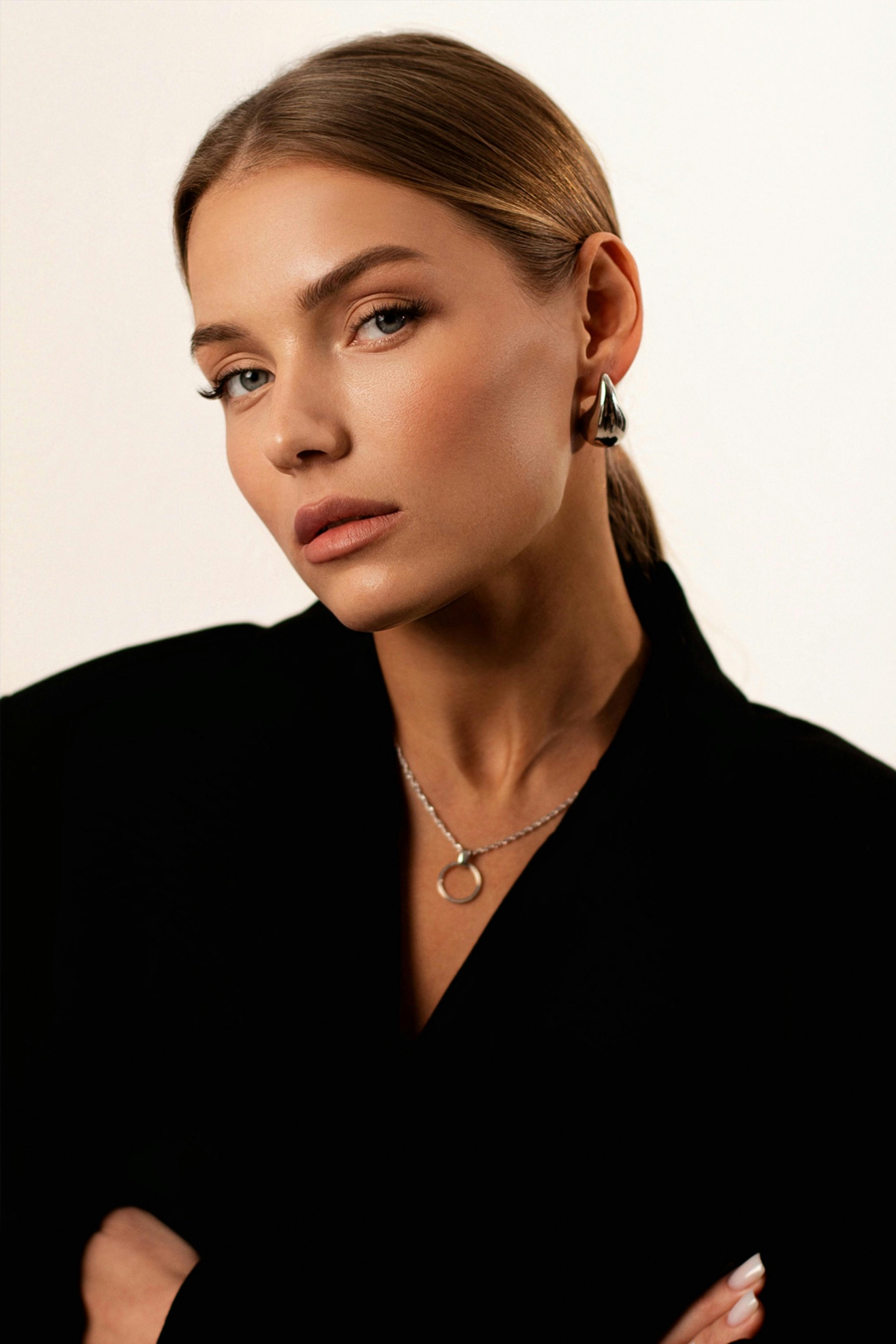 gratis Close-upportret van een elegante vrouw met neutrale gezichtsuitdrukking, gekleed in zwarte kleding en sieraden. Stockfoto