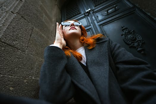 Stylish woman with sunglasses and red hair poses against an urban backdrop.
