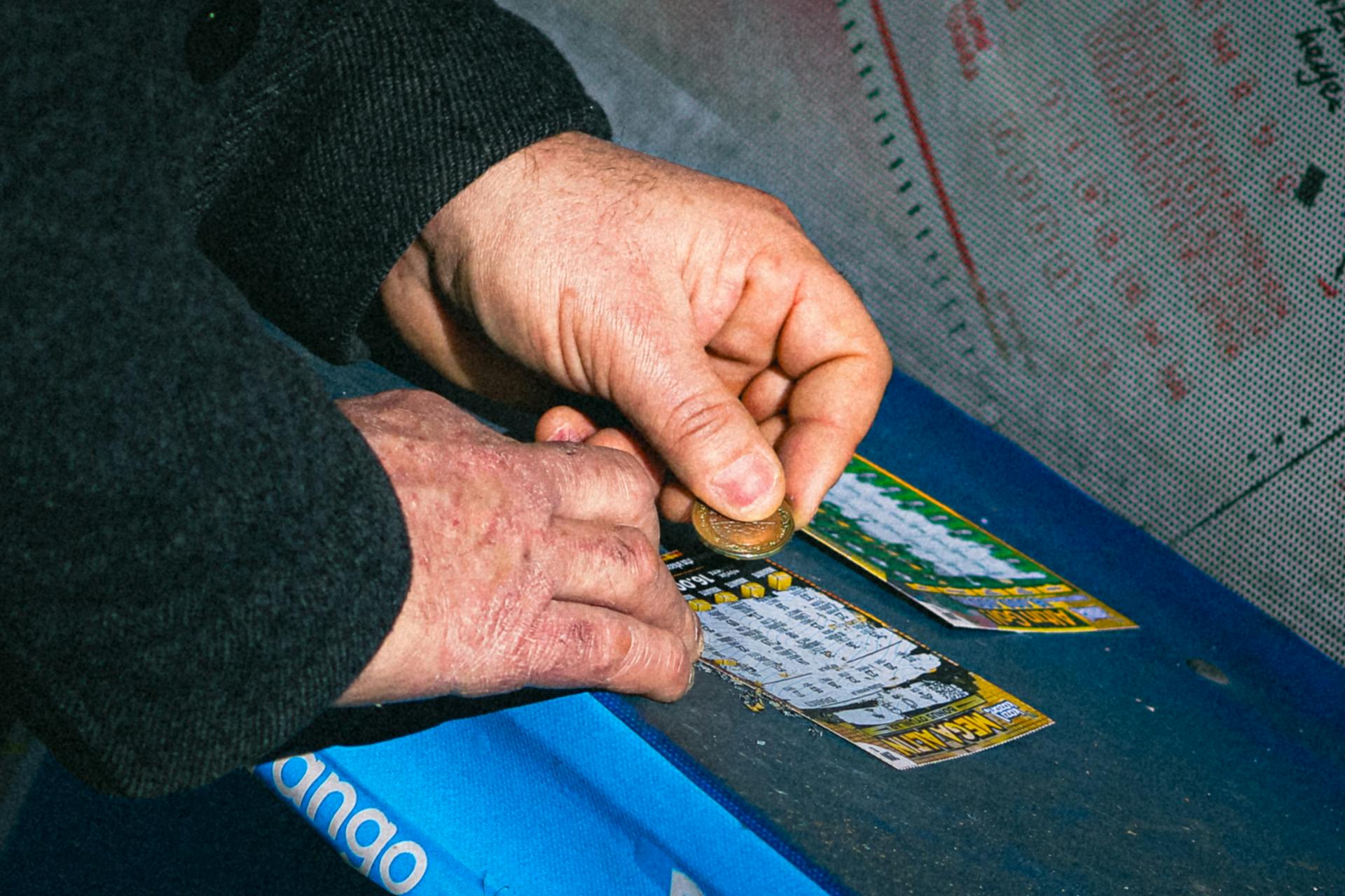 Hands using a coin to scratch off a lottery ticket on a blue table.