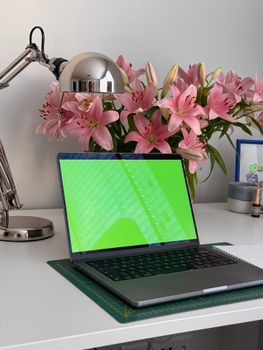 A sleek workspace featuring pink lilies and a laptop with a green screen, ideal for design mockups.